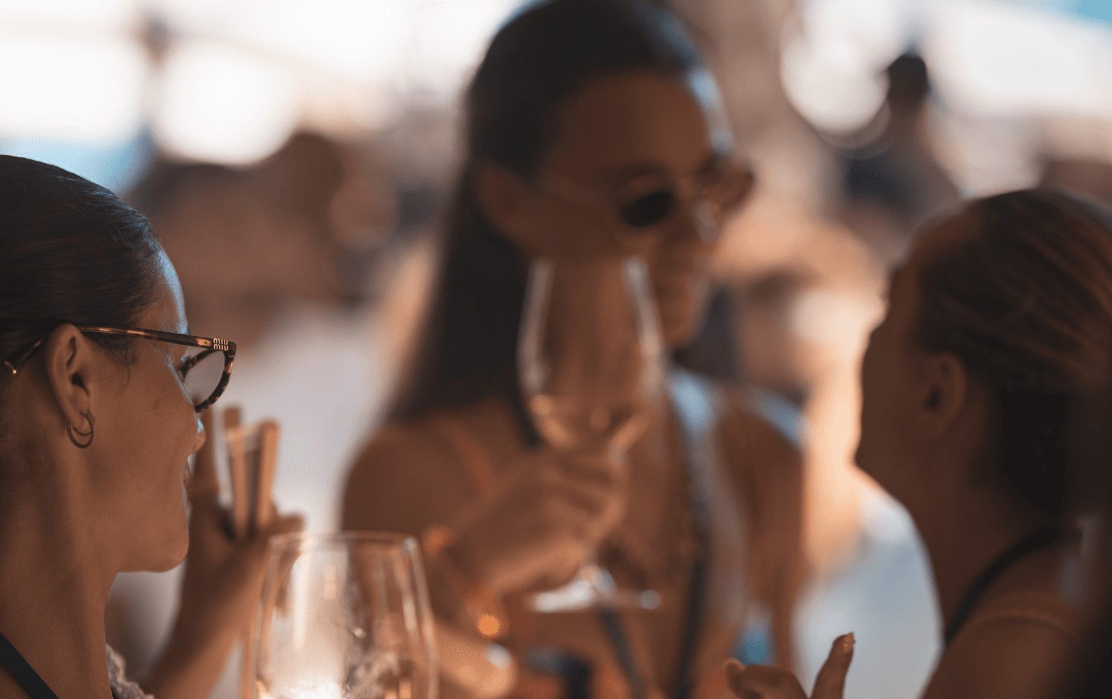 Three women are enjoying drinks and conversation at an outdoor gathering.