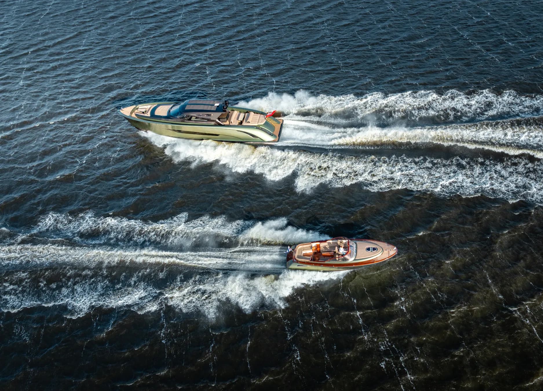 Aerial view of two luxury motorboats speeding on the water, creating white wakes against the deep blue surface.