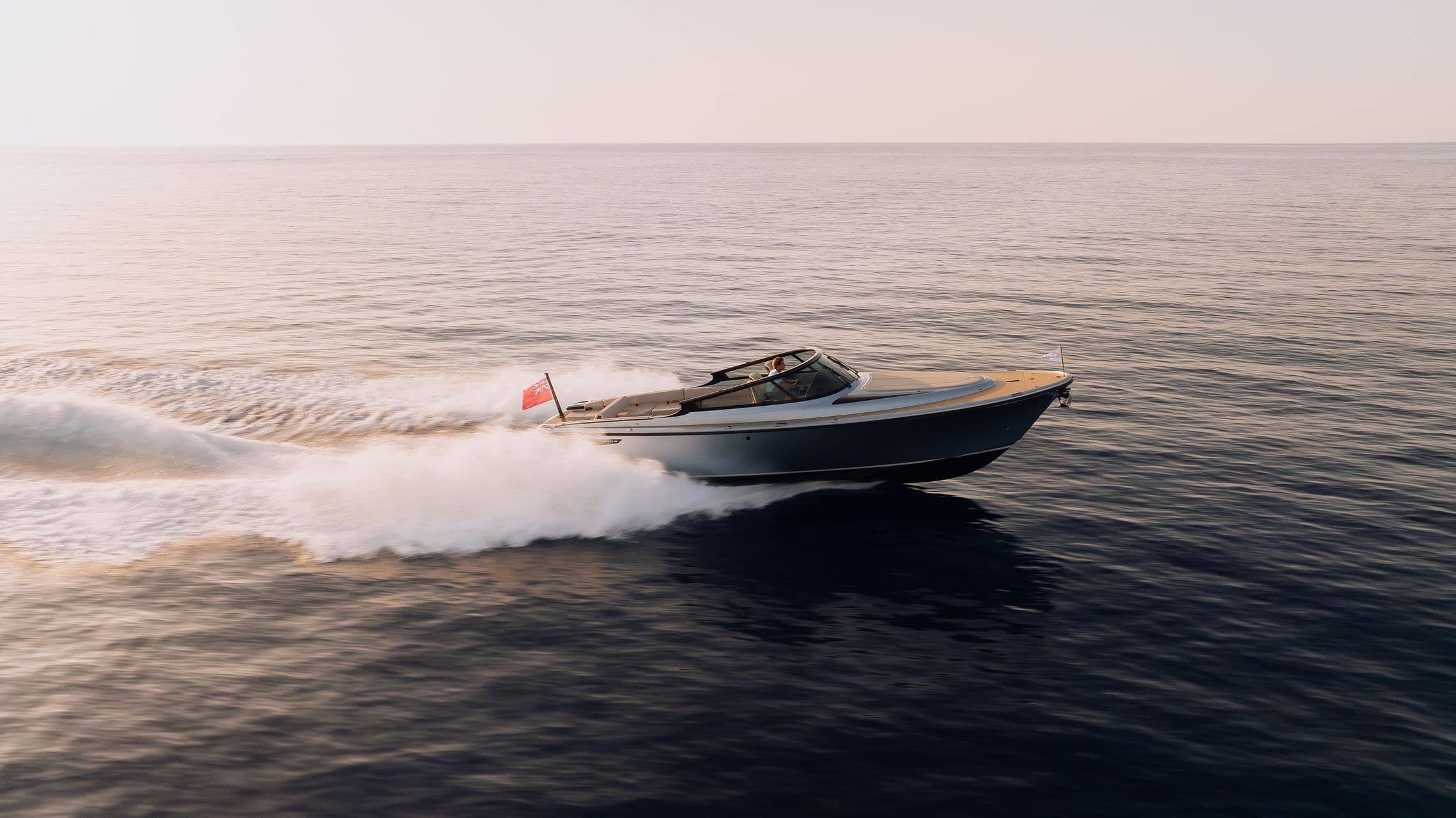 A sleek motorboat speeds across calm waters, leaving a white wake behind under a clear sky.