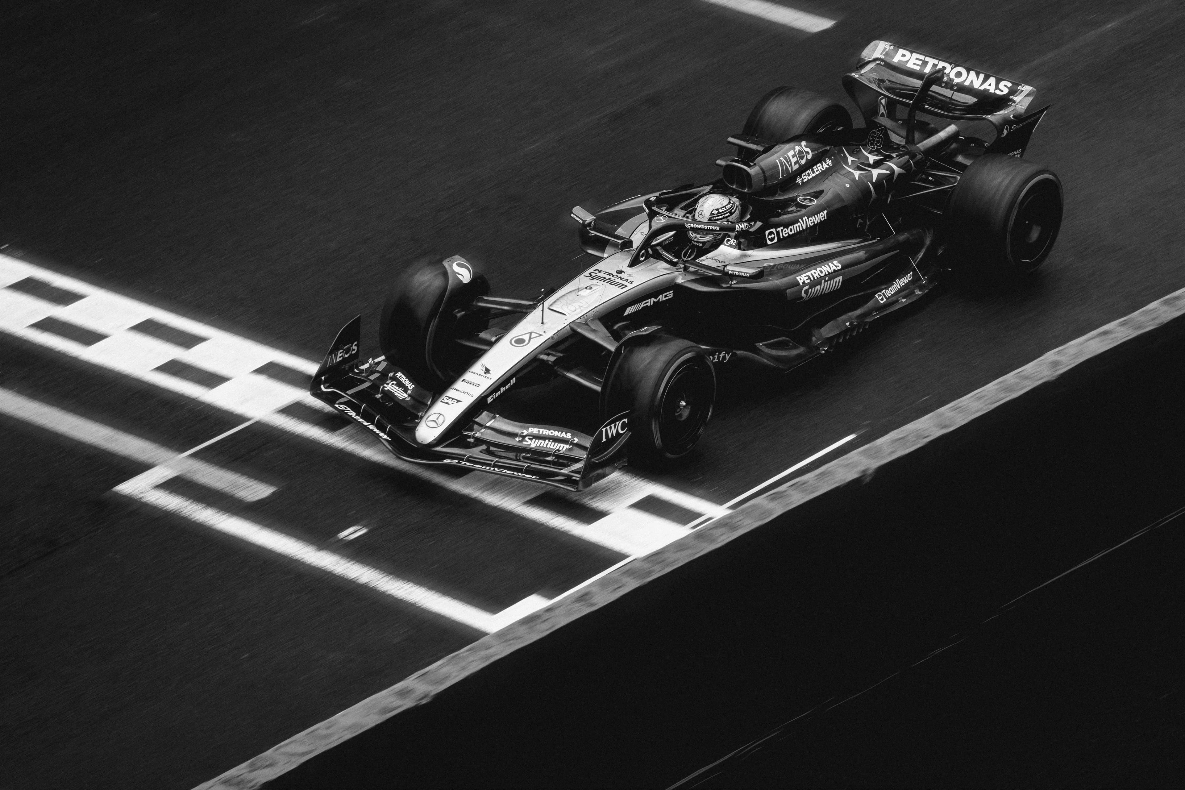 Black-and-white photo of a Formula 1 car crossing the finish line on a wet track, showing sleek design and motion blur.