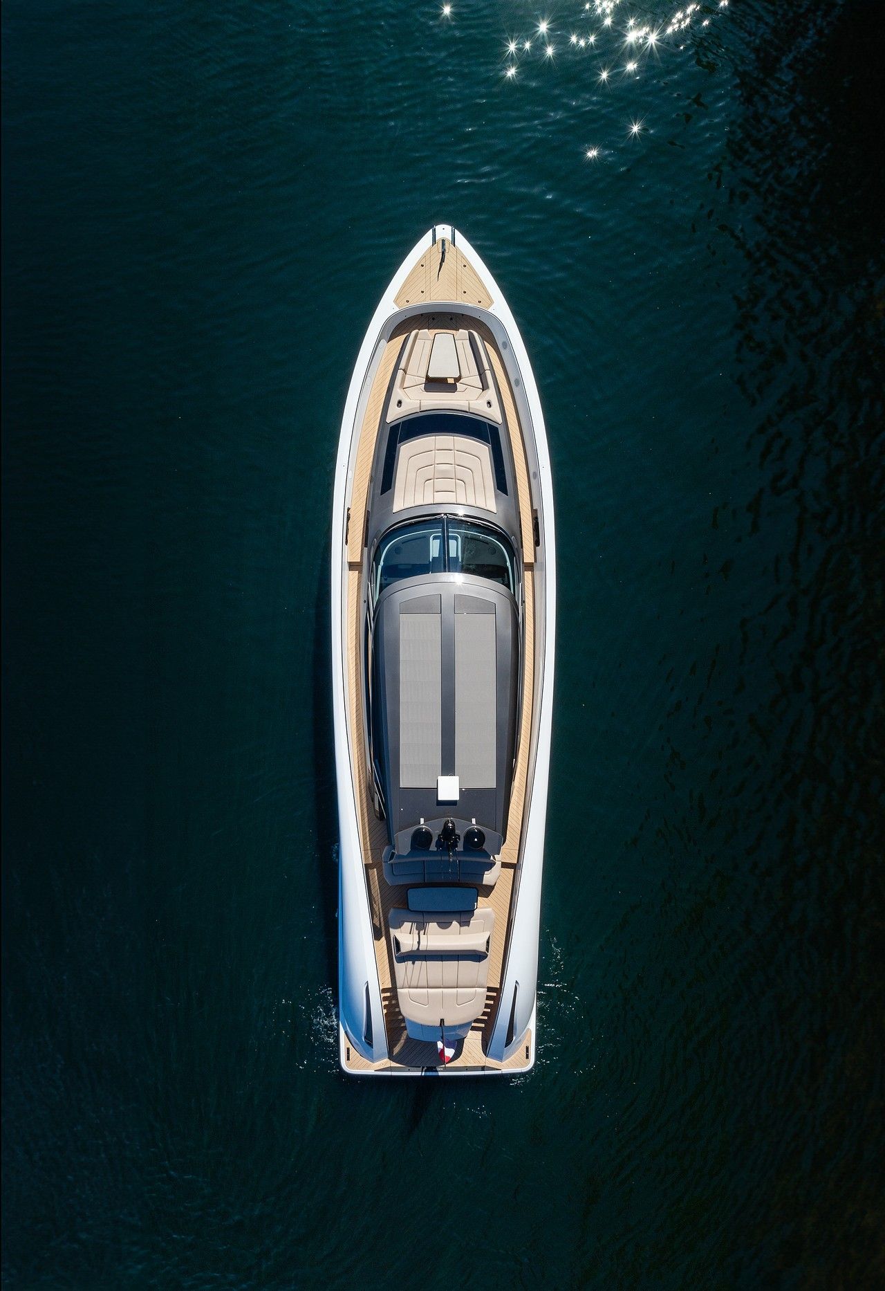 Aerial view of a luxury yacht with a sleek design cruising on clear blue water, sunlight sparkling on the surface.