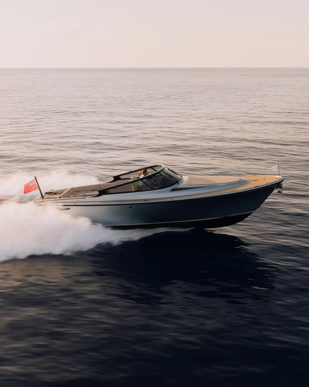 A sleek speedboat with a red flag glides over calm waters under a clear sky.