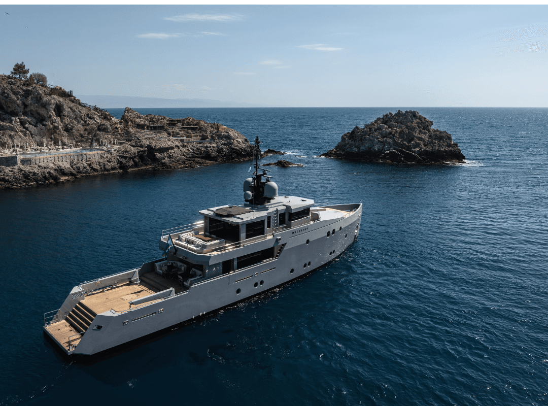 A luxurious yacht sails near rocky cliffs on a calm, blue sea under a clear sky.