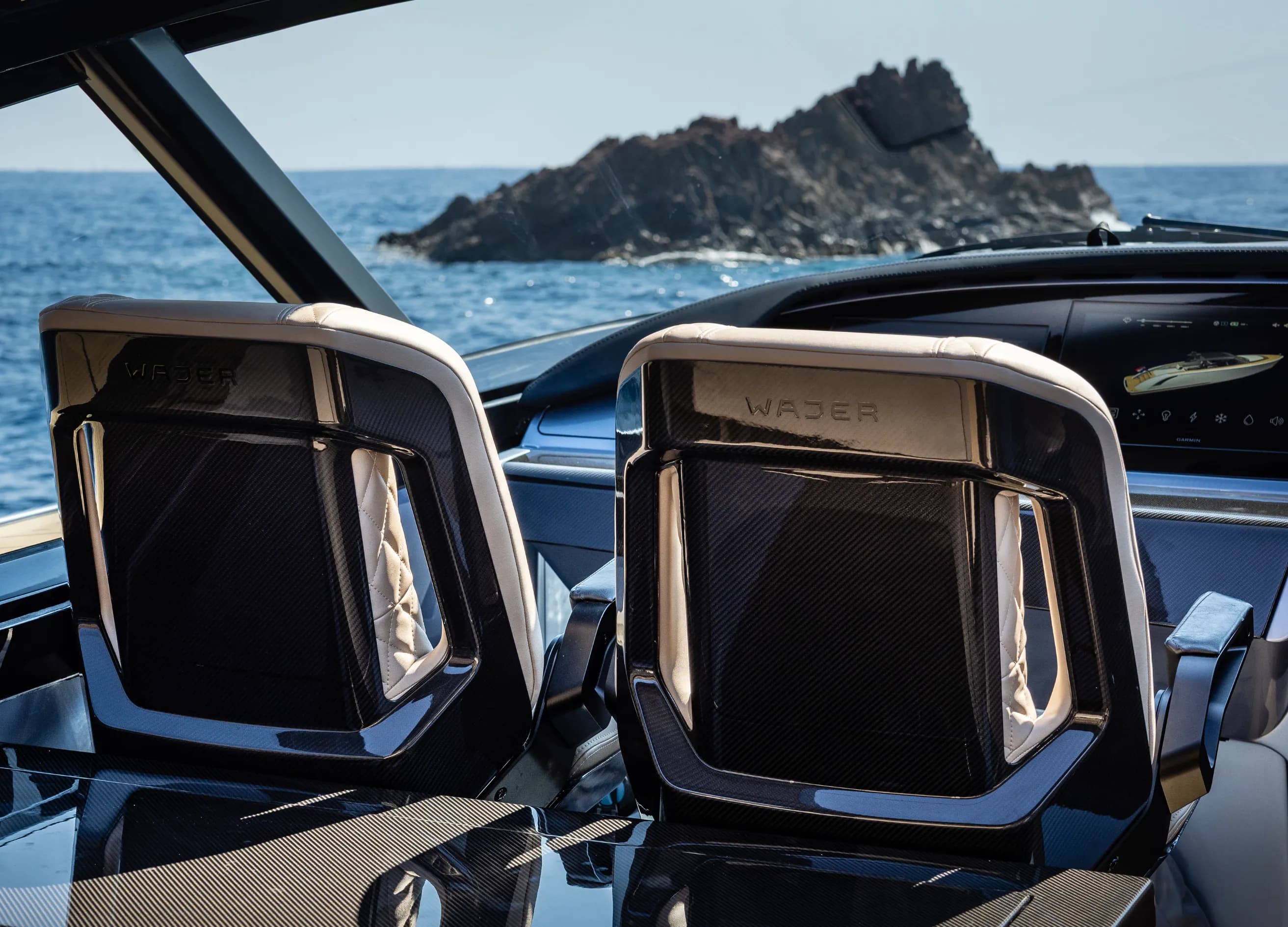 Interior view of a luxury yacht cockpit with two sleek, leather-trimmed carbon fiber seats and a navigation screen showing a boat on the open sea.