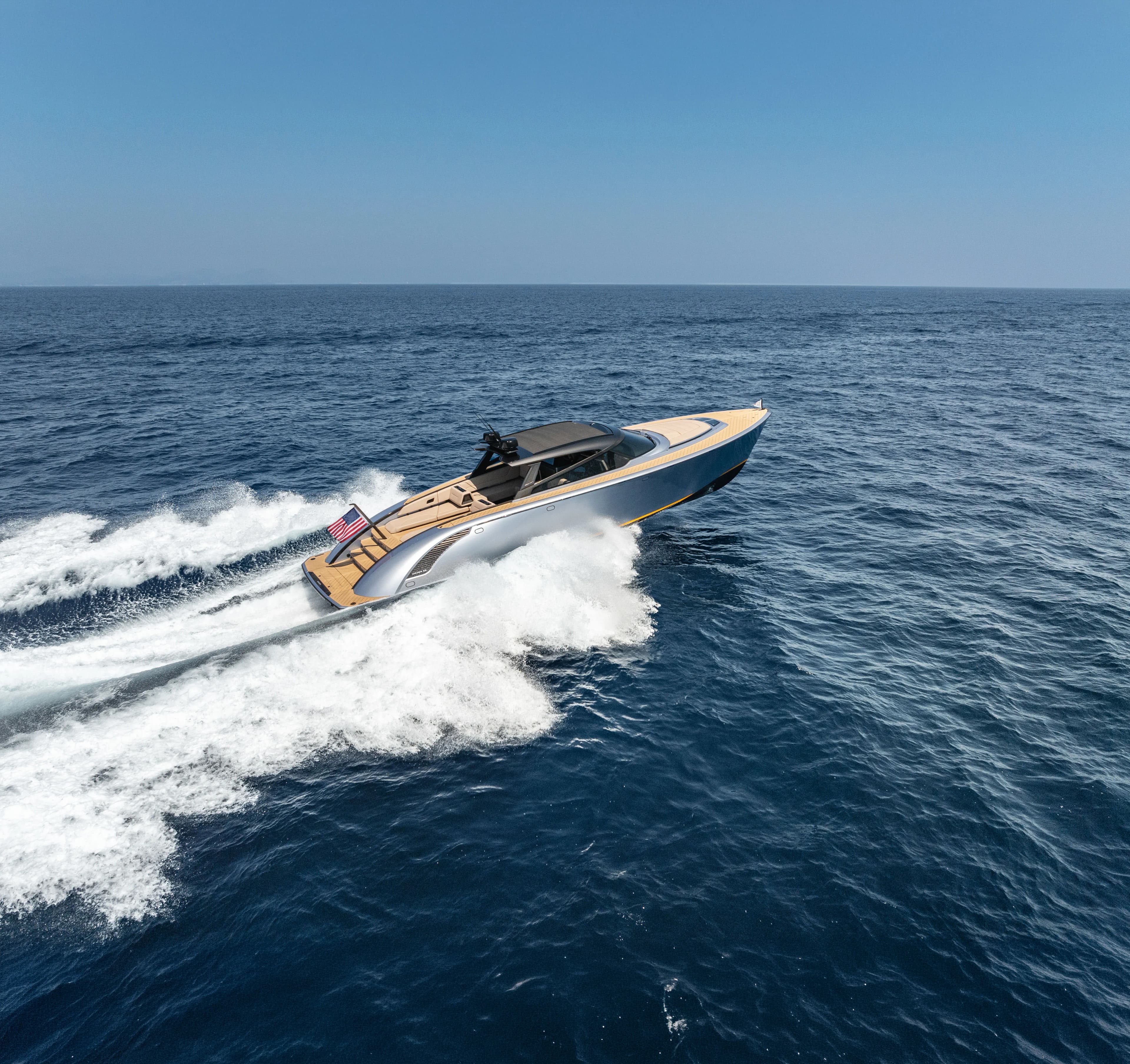 A sleek motorboat speeds across the ocean, leaving a frothy wake. A flag flutters at the stern against a clear blue sky.