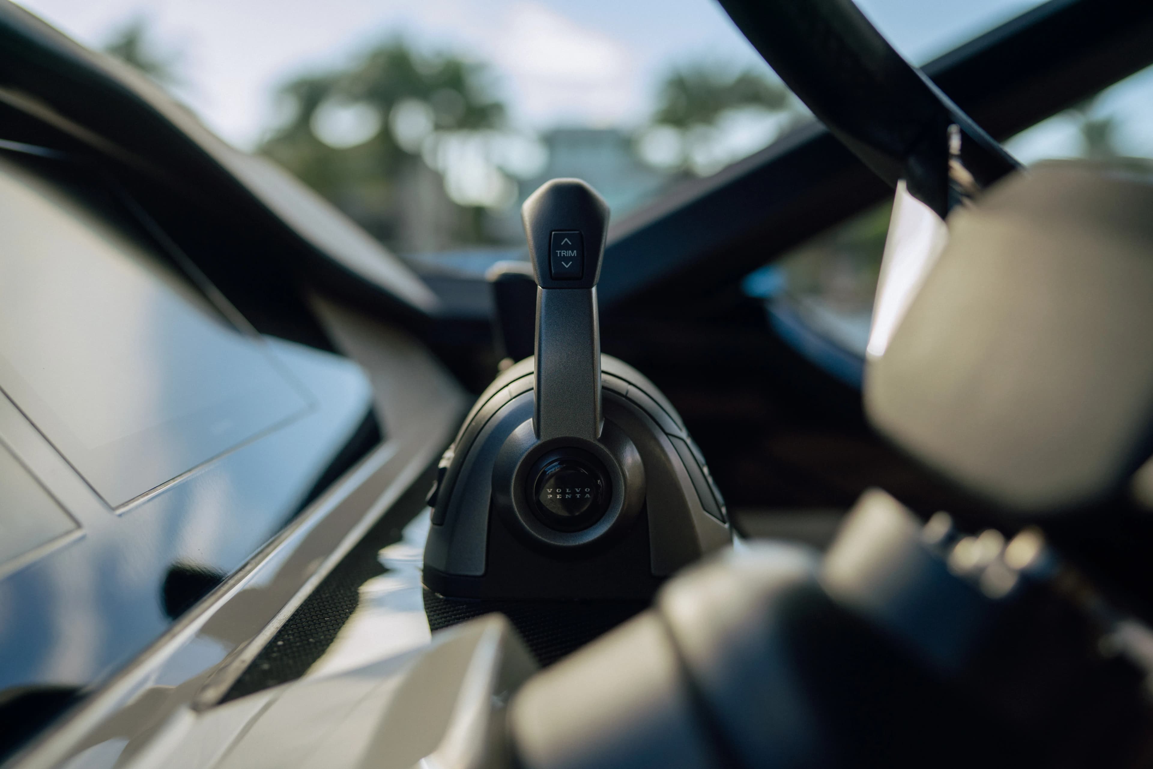 Close-up of a boat's control throttle lever labeled "Trim," with a steering wheel partially visible in the background.
